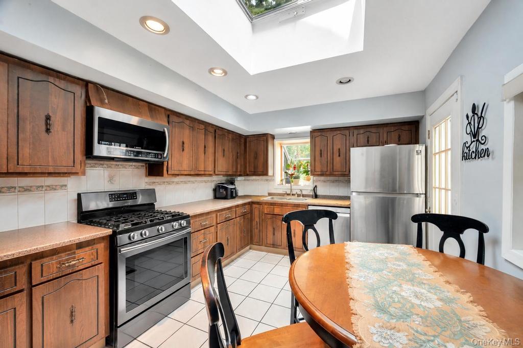 89-13 84th Street Queens, NY 11421 - Photo 18 of 34 Kitchen featuring abundant wood cabinetry, recessed lighting, a skylight, stainless steel appliances, and tile flooring