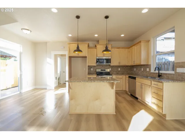 a kitchen with stainless steel appliances kitchen island granite countertop a stove a sink a refrigerator and white cabinets with wooden floor