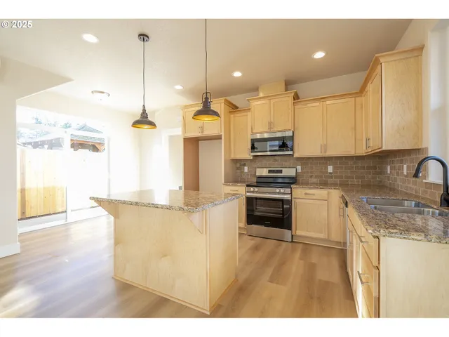 a kitchen with stainless steel appliances granite countertop a sink a stove and a wooden floor