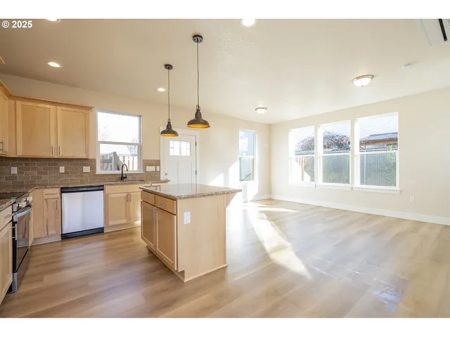 a large kitchen with kitchen island granite countertop a stove a sink a refrigerator and white cabinets with wooden floor