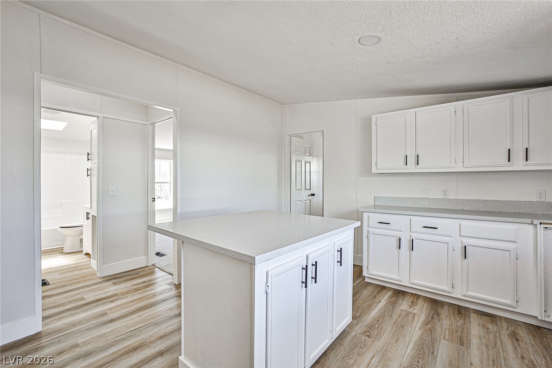 273 Aztec Lane Henderson, NV 89015 - Photo 6 of 28 A well-lit kitchen with sleek white cabinetry and a practical island, featuring durable laminate flooring.
