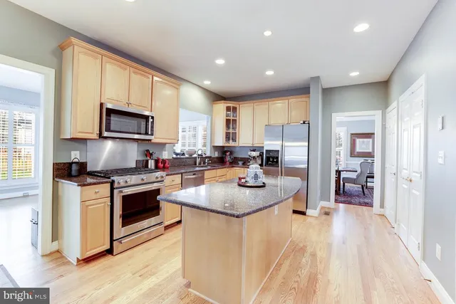 a kitchen with stainless steel appliances granite countertop a stove top oven a sink dishwasher a refrigerator and a dining table with wooden floor
