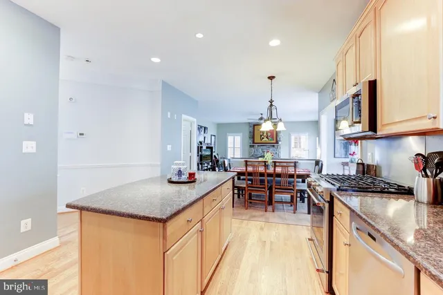 a kitchen with stainless steel appliances granite countertop a stove top oven a sink a dining table and chairs with wooden floor