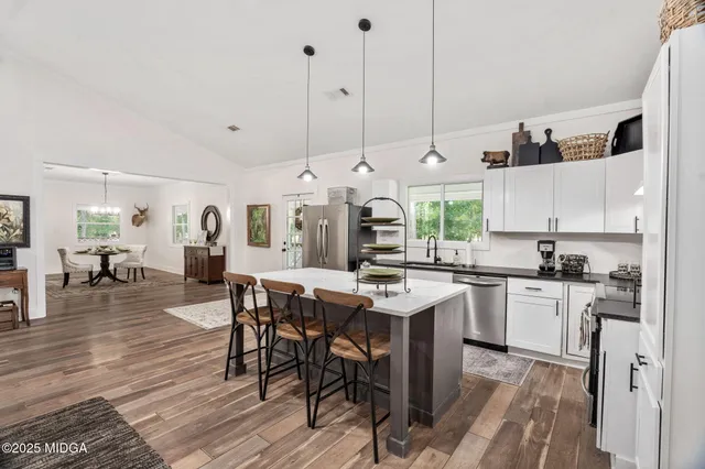 a open kitchen with stainless steel appliances granite countertop a stove top oven a refrigerator a sink dishwasher and white cabinets with wooden floor