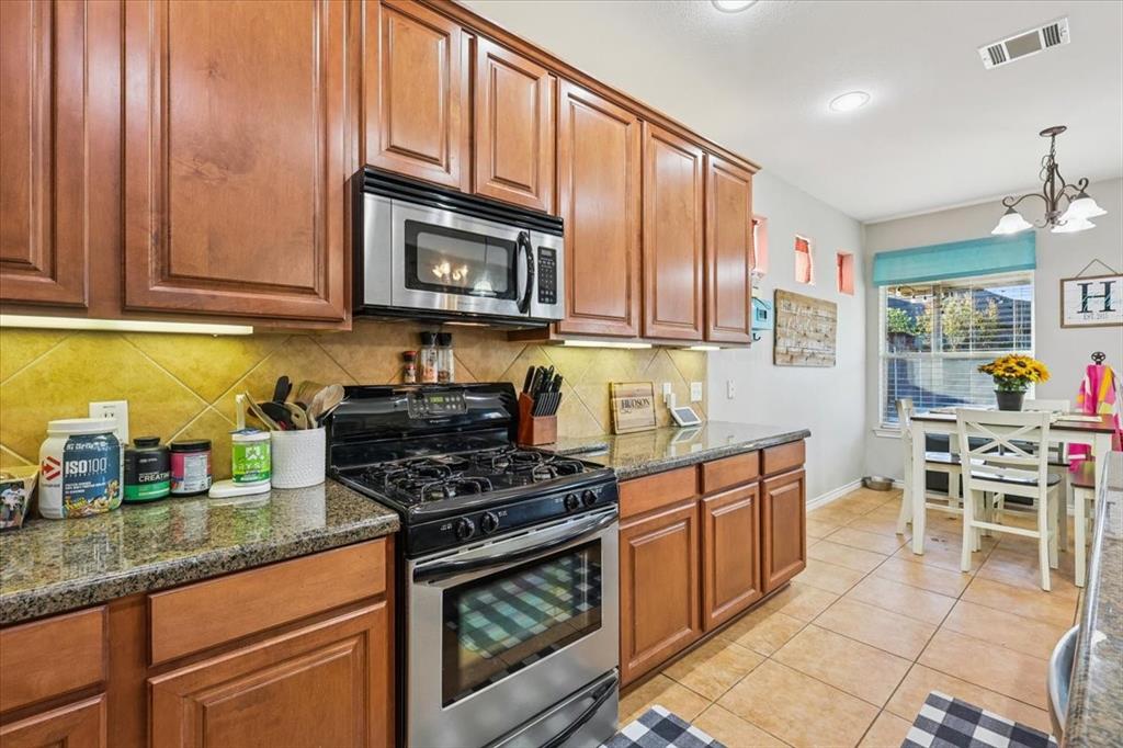 868 Valley Ridge Road Burleson, TX 76028 - Photo 9 of 39 a kitchen with stainless steel appliances granite countertop a stove top oven a sink a dining table and chairs with wooden cabinets