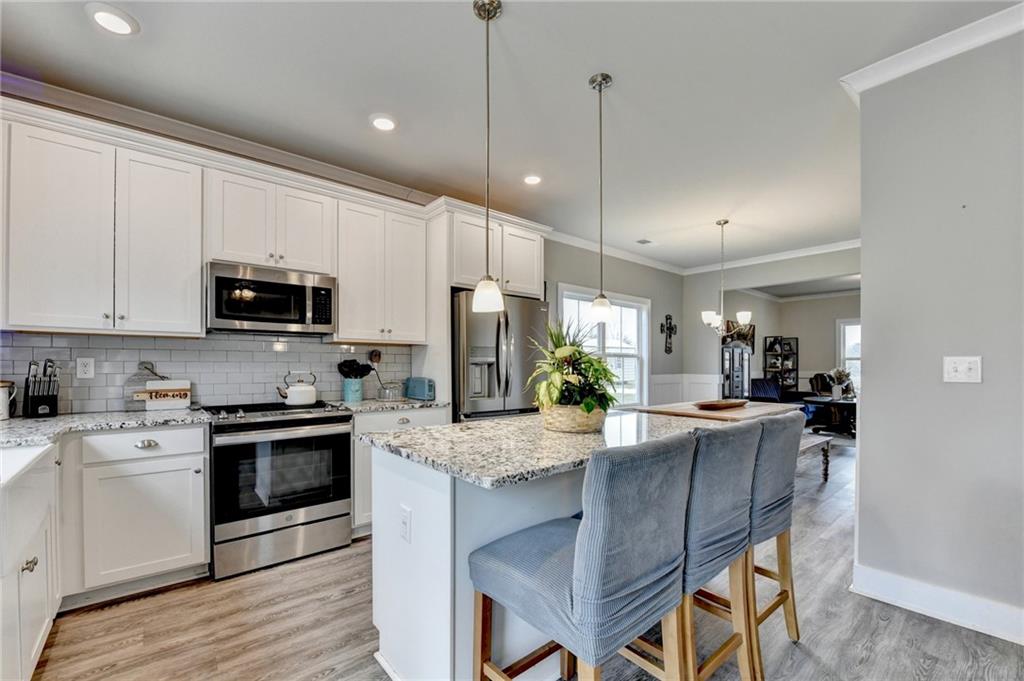 1179 Simmons Road Social Circle, GA 30025 - Photo 17 of 71 a kitchen with kitchen island granite countertop a stove a sink a microwave a refrigerator and white cabinets with wooden floor