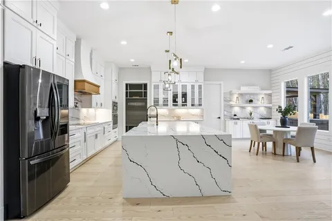 a kitchen with stainless steel appliances kitchen island granite countertop a refrigerator a stove a sink a dining table and chairs with wooden floor