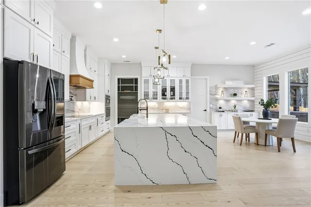 a kitchen with stainless steel appliances kitchen island granite countertop a refrigerator a stove a sink a dining table and chairs with wooden floor