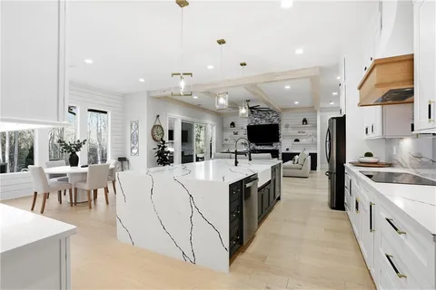 a large open kitchen with stainless steel appliances kitchen island a stove a refrigerator a dining table and chairs with wooden floor