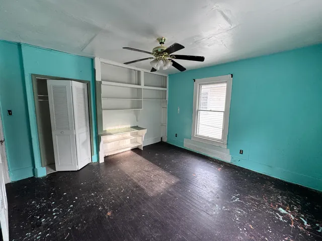an empty room with wooden floor chandelier fan and windows