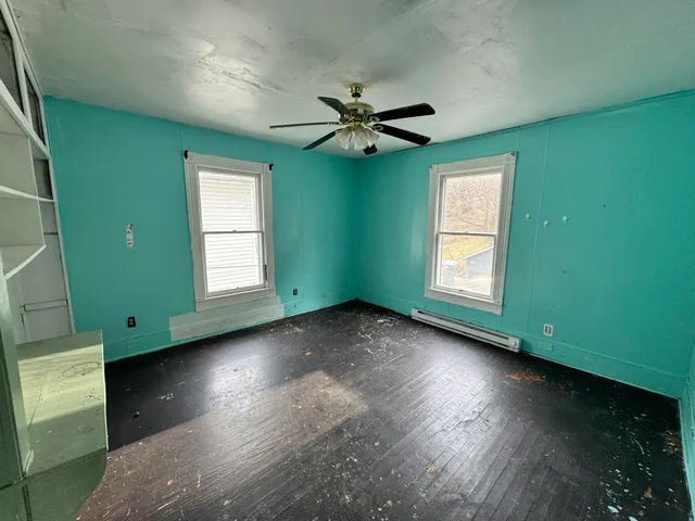 an empty room with wooden floor fan and windows