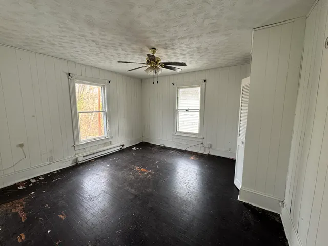 an empty room with wooden floor chandelier fan and windows
