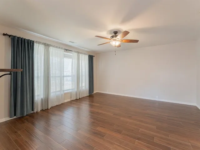 an empty room with wooden floor chandelier fan and windows