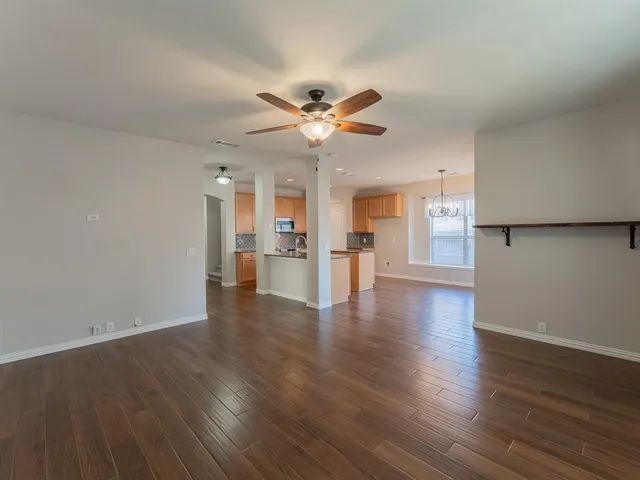 a view of an empty room with wooden floor and a ceiling fan