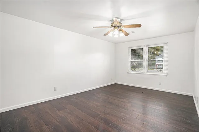 an empty room with wooden floor chandelier fan and windows