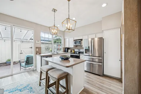 a kitchen with stainless steel appliances a refrigerator a stove a sink dishwasher a dining table and chairs with wooden floor