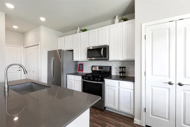 a kitchen with stainless steel appliances granite countertop a stove top oven a sink dishwasher a dining table and chairs with wooden floor