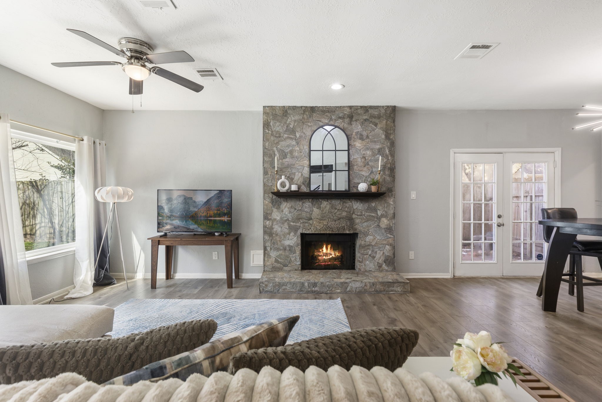 2110 Paso Rello Drive Houston, TX 77077 - Photo 10 of 41 This inviting living room features a cozy stone fireplace, large windows with natural light. The open layout flows into a dining area with French doors leading outside, perfect for entertaining.