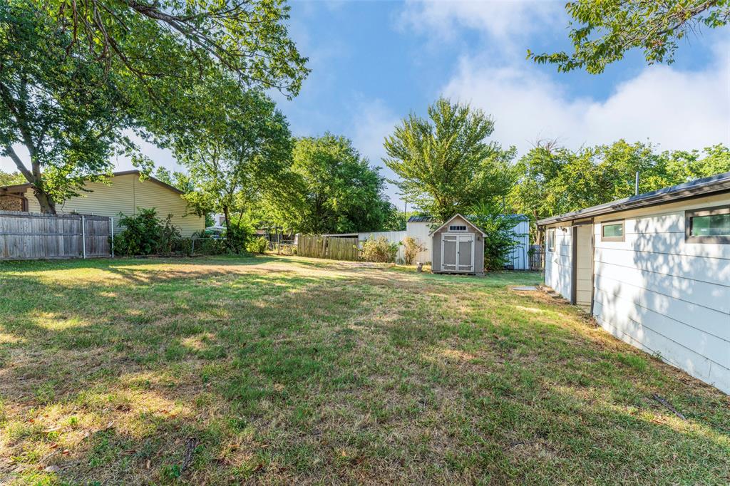 310 North Road Kennedale, TX 76060 - Photo 2 of 23 Expansive outdoor area featuring a storage shed, white exterior building, and mature trees