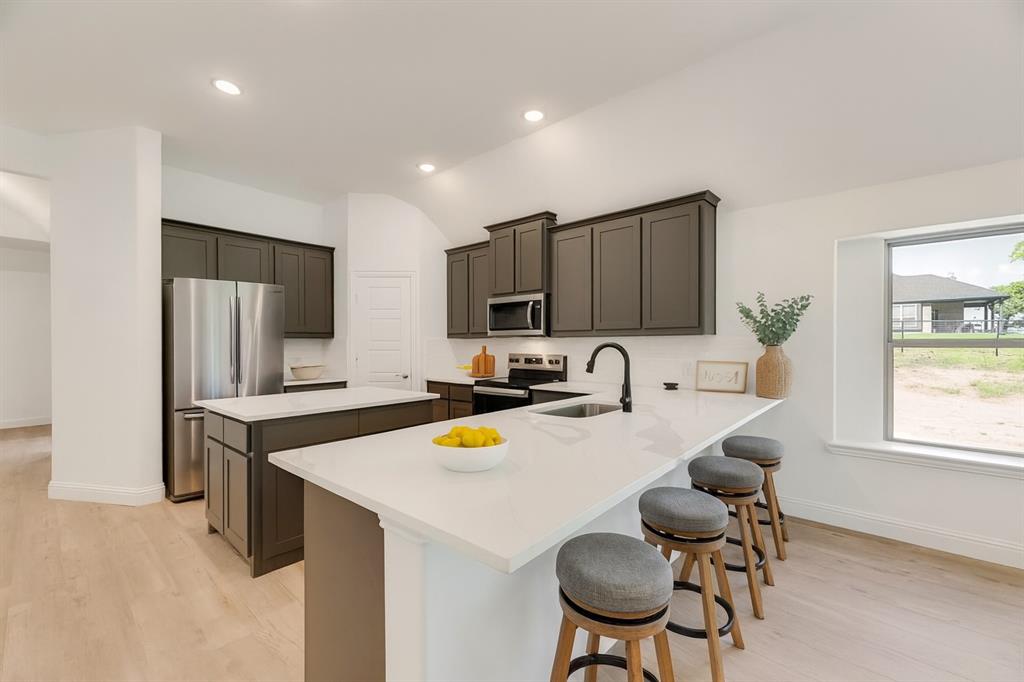 128 Loveta Lane Boyd, TX 76023 - Photo 3 of 15 a kitchen with a refrigerator a stove a dining table and chairs with wooden floor