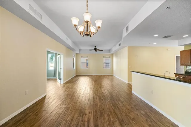 a view of an empty room with wooden floor and kitchen view