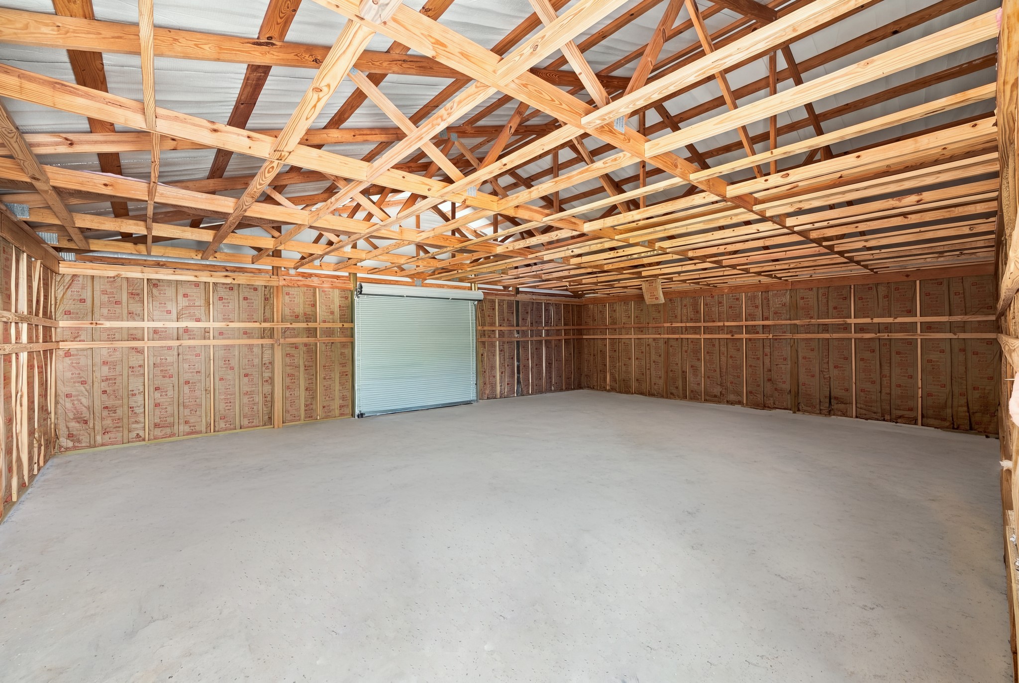 7049 Pine Shadows Road Cleveland, TX 77328 - Photo 34 of 49 Spacious unfinished garage with high ceilings, exposed wooden beams, and a large roll-up door, offering ample storage or workshop potential.
