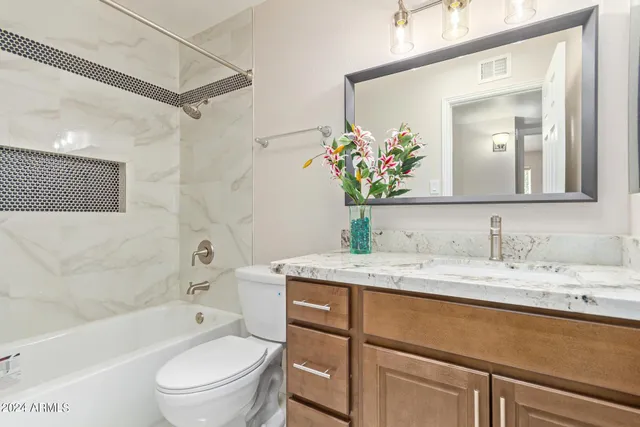 a bathroom with a granite countertop sink vanity mirror bathtub shower and a toilet