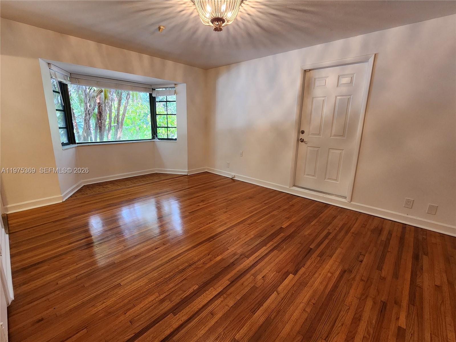 6065 Southwest 133rd Street Pinecrest, FL 33156 - Photo 18 of 41 an empty room with wooden floor chandelier fan and windows