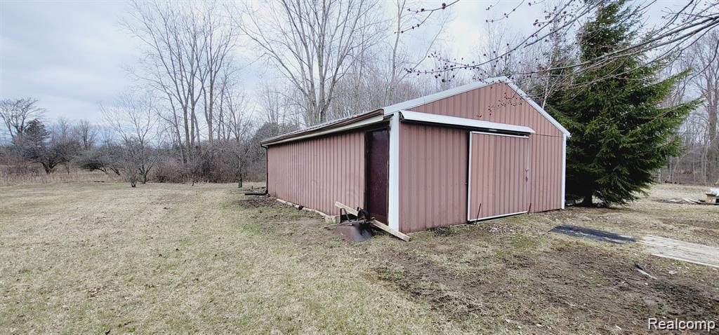 2611 Miller Road Allenton, MI 48002 - Photo 19 of 41 Metal-sided outbuilding with an overhang, featuring a large sliding door and a standard entry door, set on a grass lot
