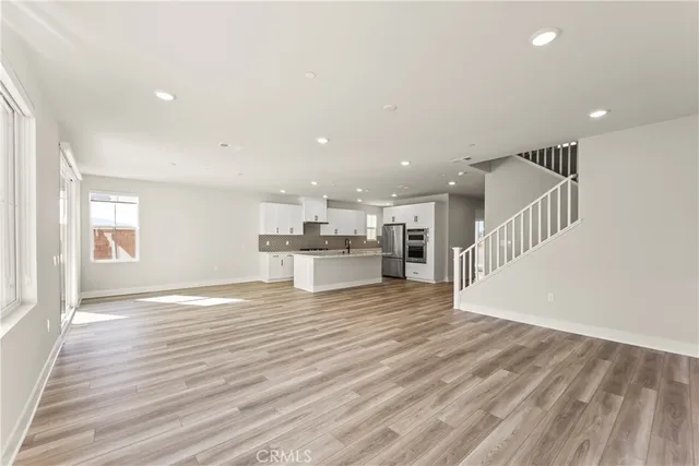 an empty room with wooden floor and a kitchen