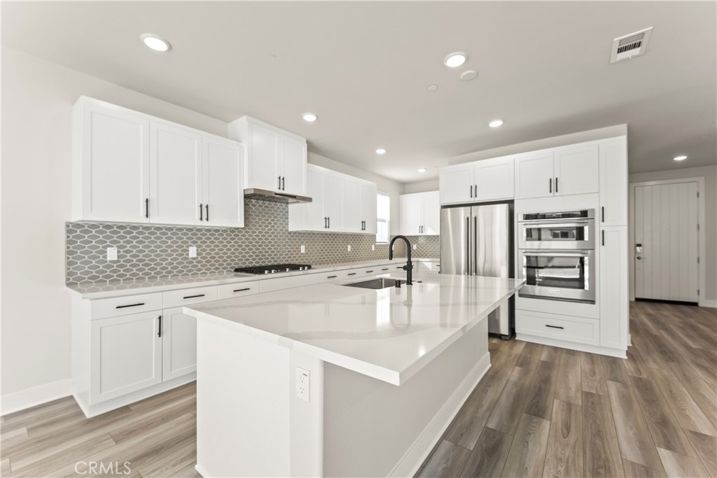 16717 Dara Avenue Chino, CA 91708 - Photo 18 of 41 a large kitchen with kitchen island a stove a sink a refrigerator and white cabinets with wooden floor