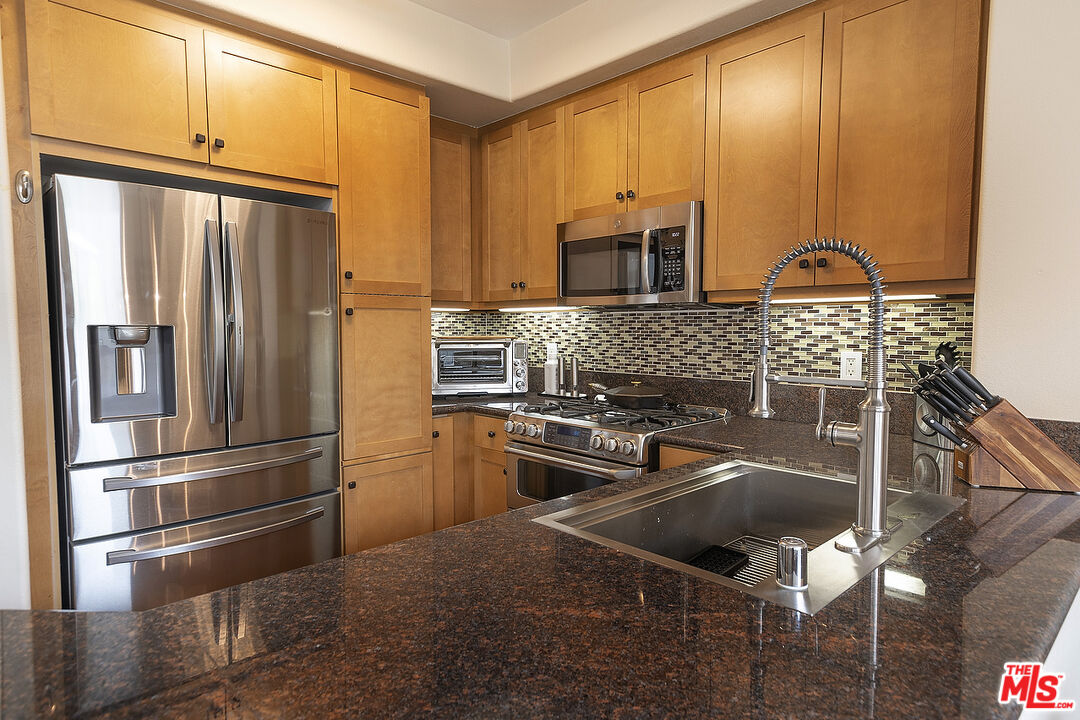 13044 Pacific Promenade, Unit 419 Playa Vista, CA 90094 - Photo 7 of 19 a kitchen with stainless steel appliances granite countertop a refrigerator a stove and a sink with wooden cabinets