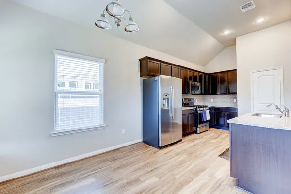 a kitchen with stainless steel appliances granite countertop a refrigerator a sink dishwasher a stove and a dining table with wooden floor