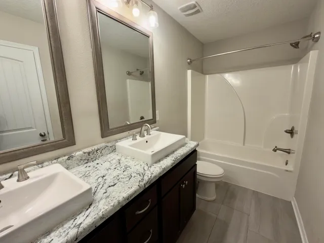 a bathroom with a granite countertop sink a toilet a mirror and shower