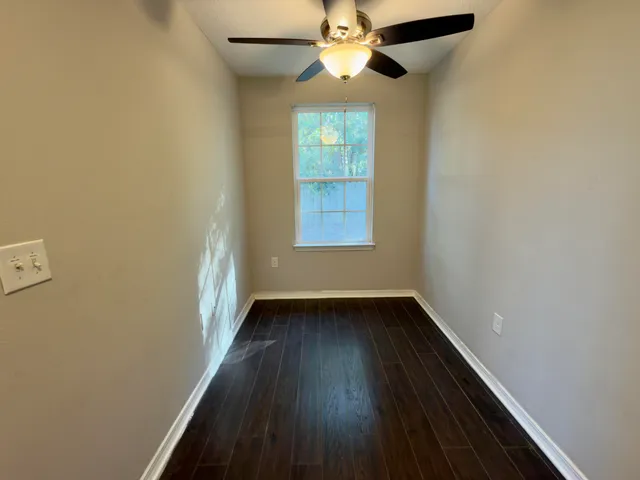 an empty room with wooden floor fan and windows