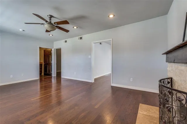 a view of an empty room with wooden floor and a ceiling fan