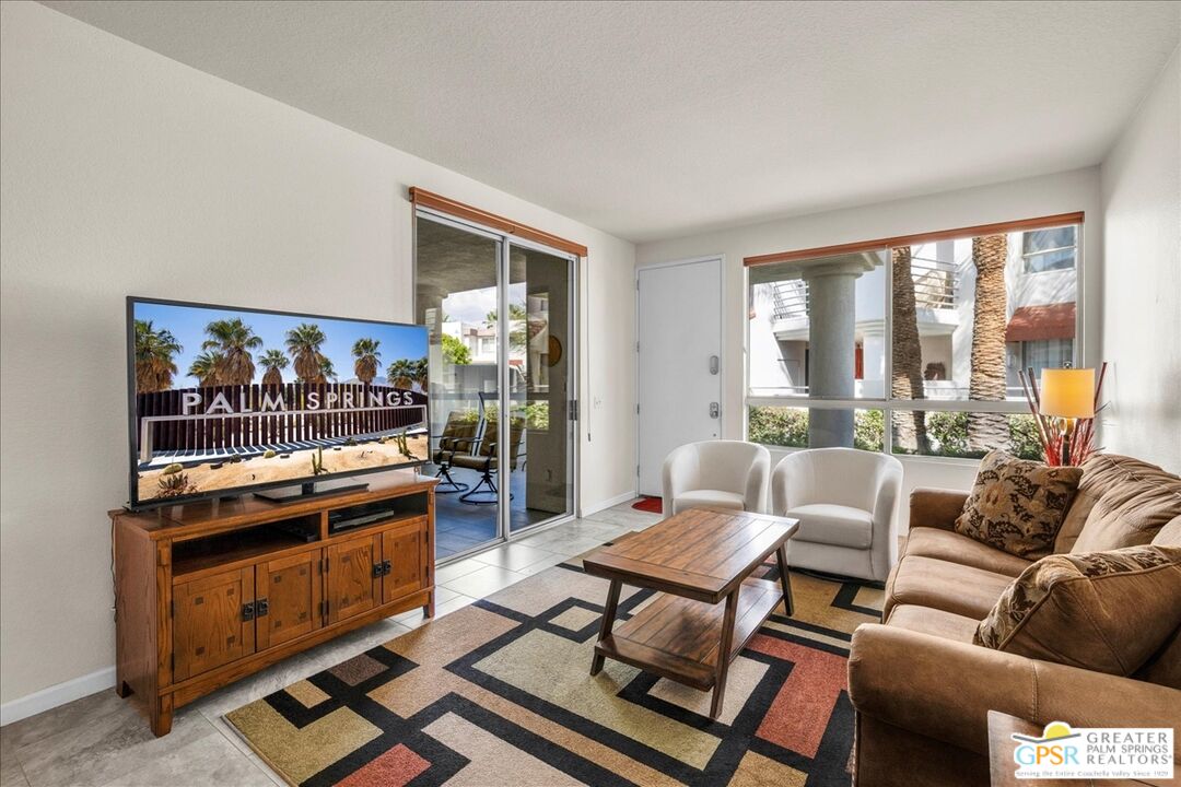 401 El Cielo Road, Unit 147 Palm Springs, CA 92262 - Photo 8 of 44 a living room with furniture a flat screen tv and a floor to ceiling window