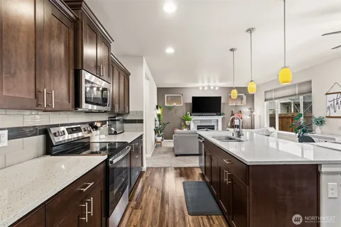 a open kitchen with stainless steel appliances granite countertop a stove top oven a sink dishwasher a dining table and chairs with wooden floor