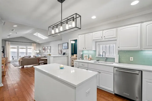 a kitchen with a sink dishwasher a stove and white cabinets with wooden floor