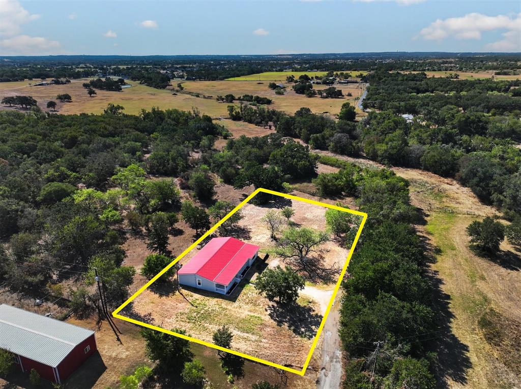 795 Meadow Road Springtown, TX 76082 - Photo 23 of 27 Aerial perspective showcasing a single-story residence with a red metal roof and light-colored siding
