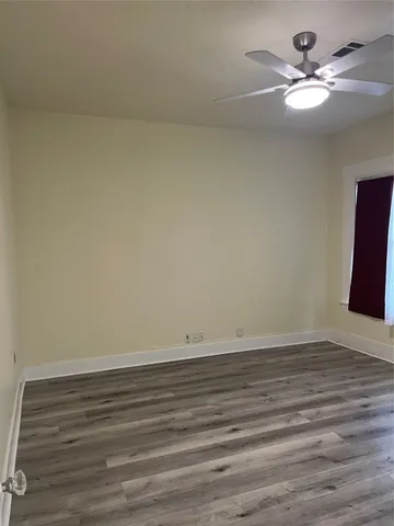 a view of an empty room with wooden floor and a ceiling fan