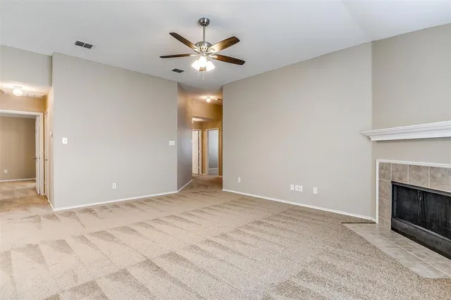 a view of an empty room with chandelier fan and fire place