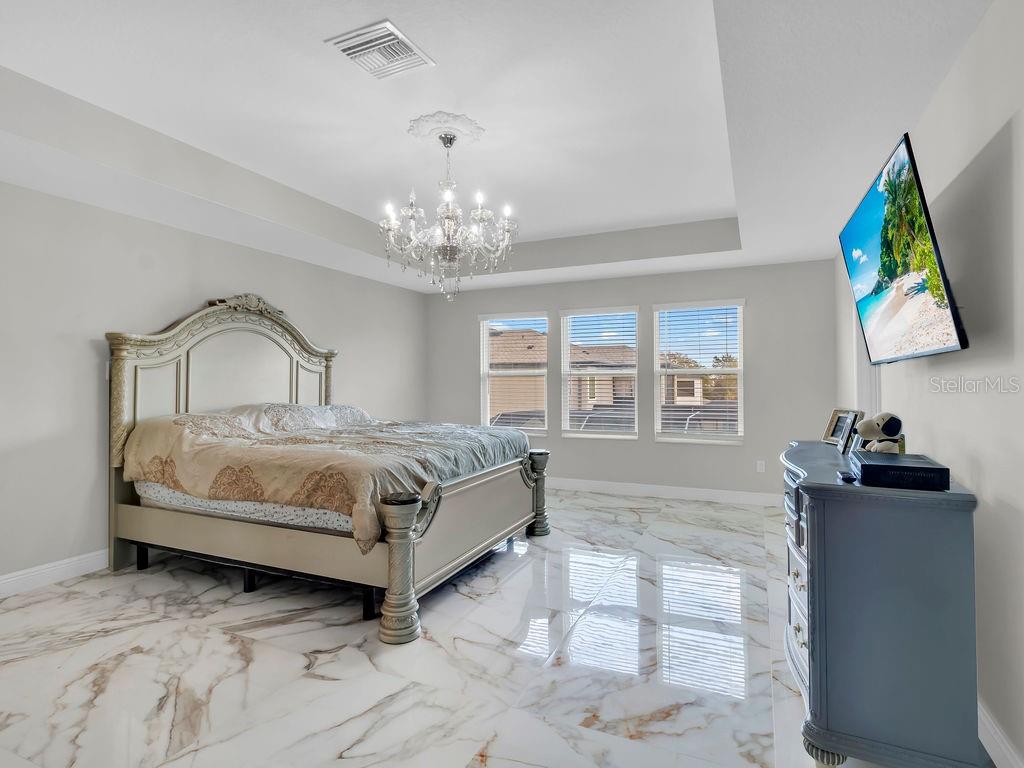 7406 Sweeter Tide Trail Wesley Chapel, FL 33545 - Photo 32 of 74 a spacious bedroom with a bed and a chandelier