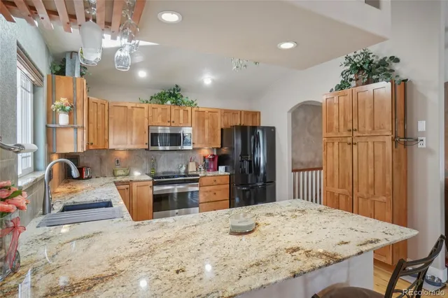 a kitchen with granite countertop a refrigerator a stove a sink dishwasher and wooden cabinets with wooden floor