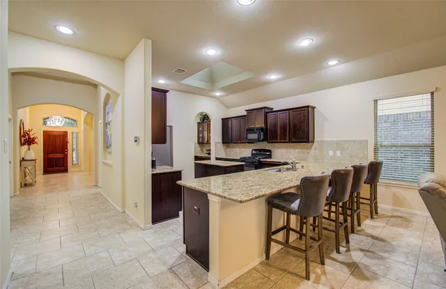 a kitchen with stainless steel appliances granite countertop a stove top oven a sink a refrigerator a dining table and chairs