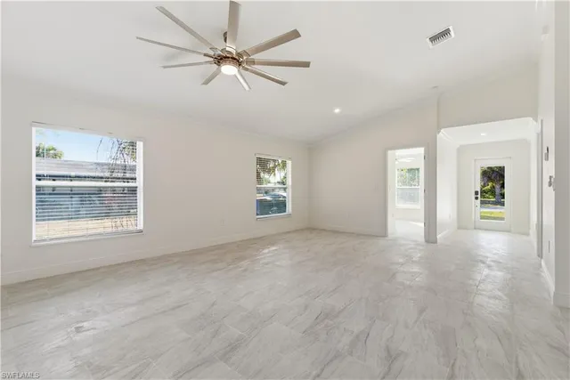 an empty room with chandelier fan and windows