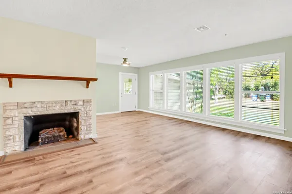 a view of an empty room with wooden floor fireplace and a window
