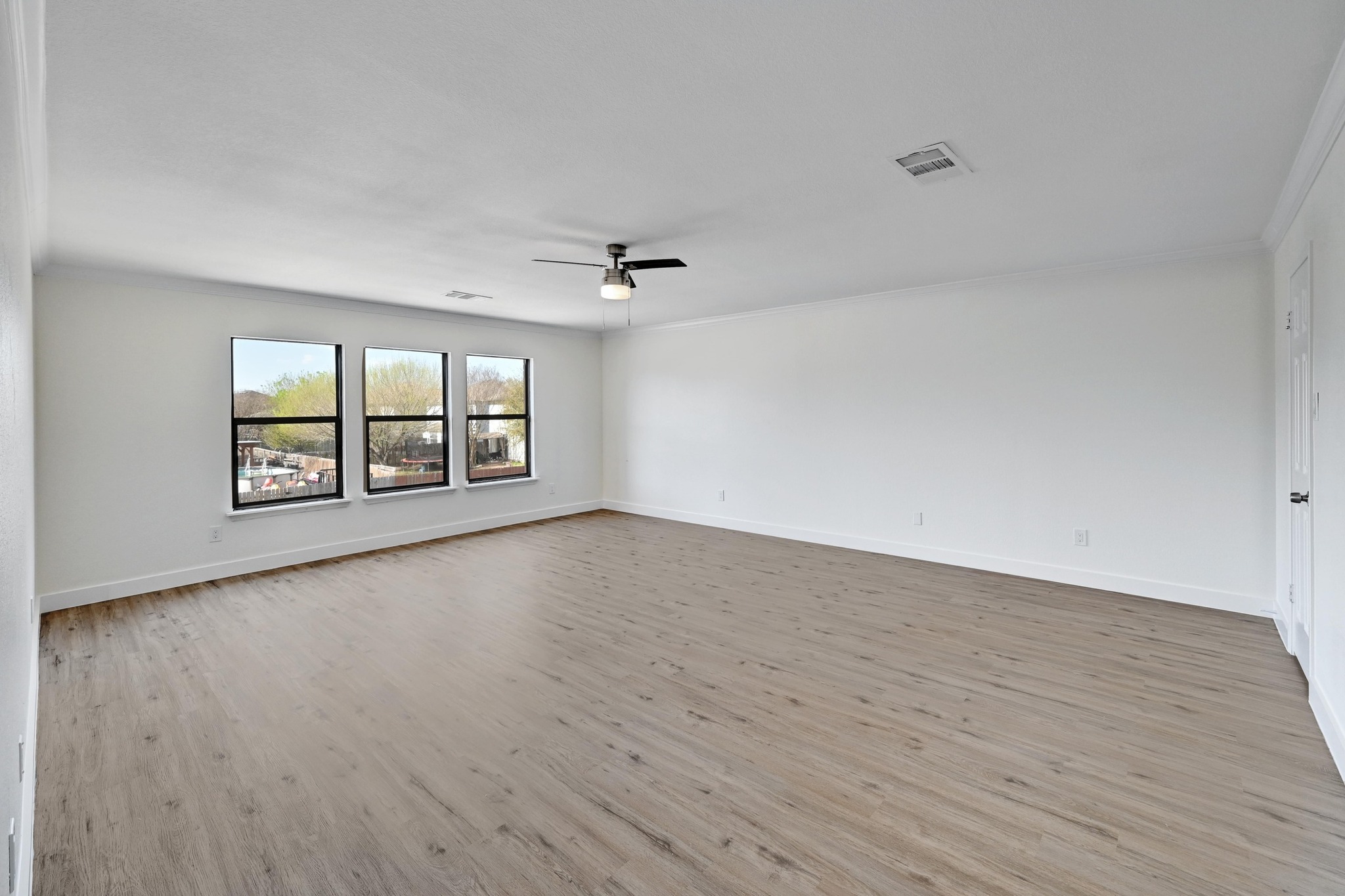 7413 L Marble Ridge Drive Austin, TX 78747 - Photo 13 of 30 Spacious room featuring light wood-finish flooring, three large windows with black frames, white walls, and a ceiling fan with integrated lighting