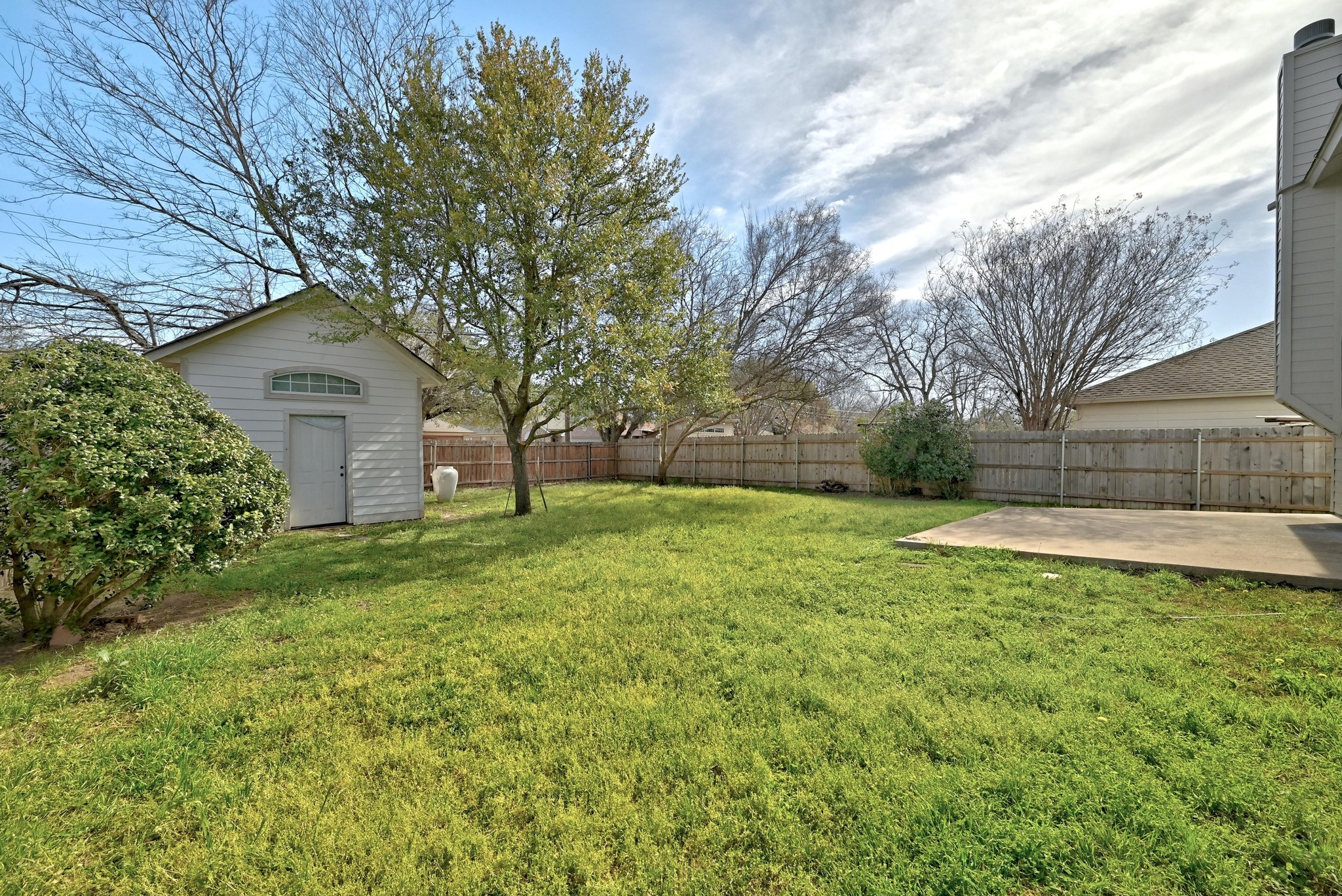 7413 L Marble Ridge Drive Austin, TX 78747 - Photo 27 of 30 Expansive backyard featuring a lush lawn, mature trees, a detached storage shed with an arched window, a concrete patio, and wood privacy fencing