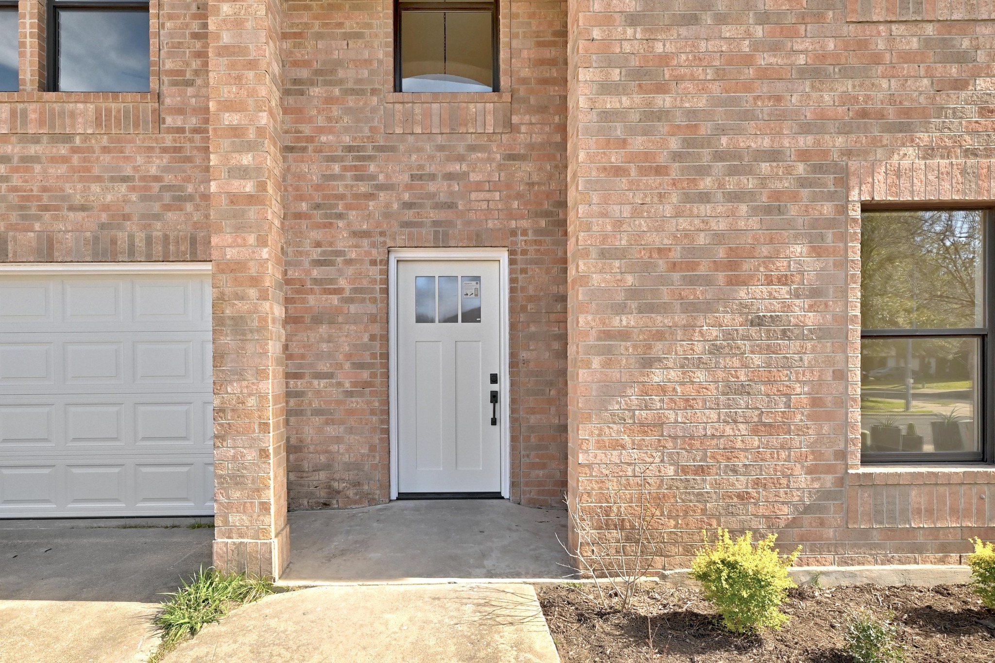 7413 L Marble Ridge Drive Austin, TX 78747 - Photo 29 of 30 Brick exterior featuring a white paneled front door with glass inserts, a white paneled garage door, and dark-framed windows